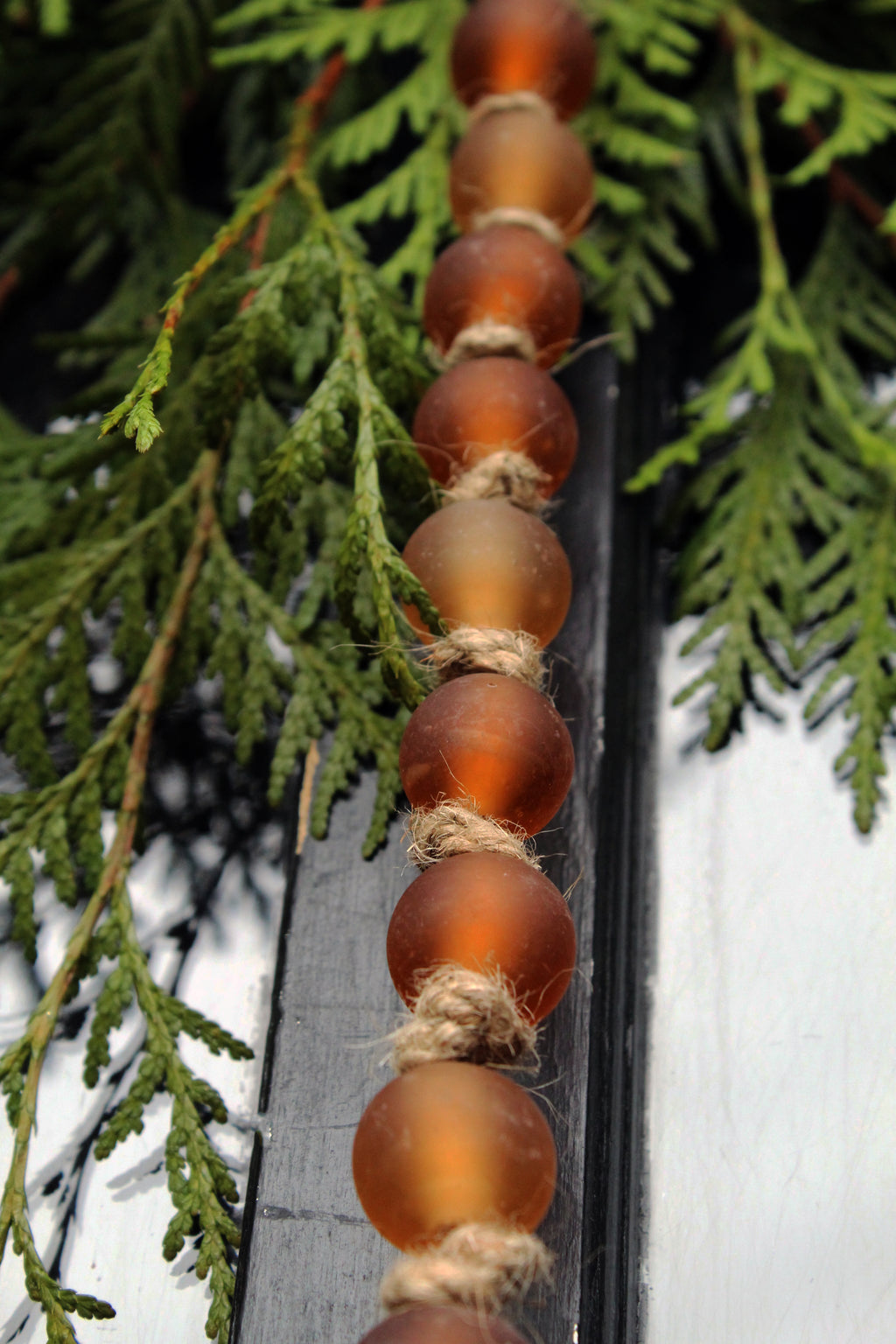 String of amber-colored beads on a rope with green foliage in the background